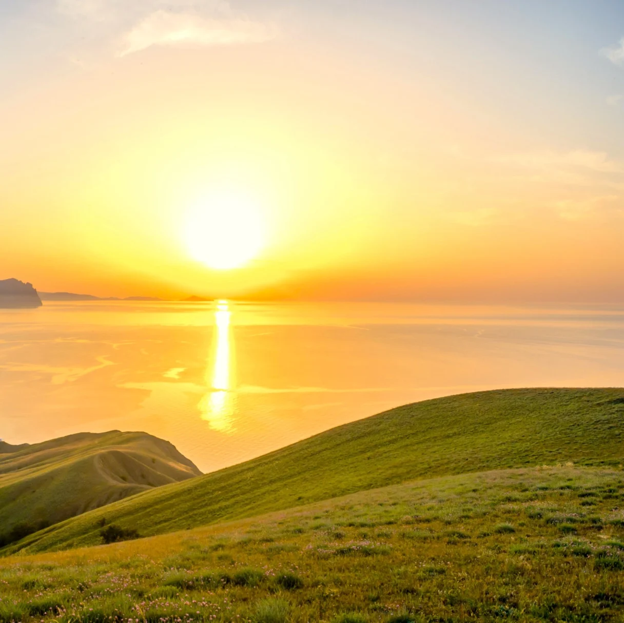 Zonsopkomst boven zee, met groene heuvels op de voorgrond